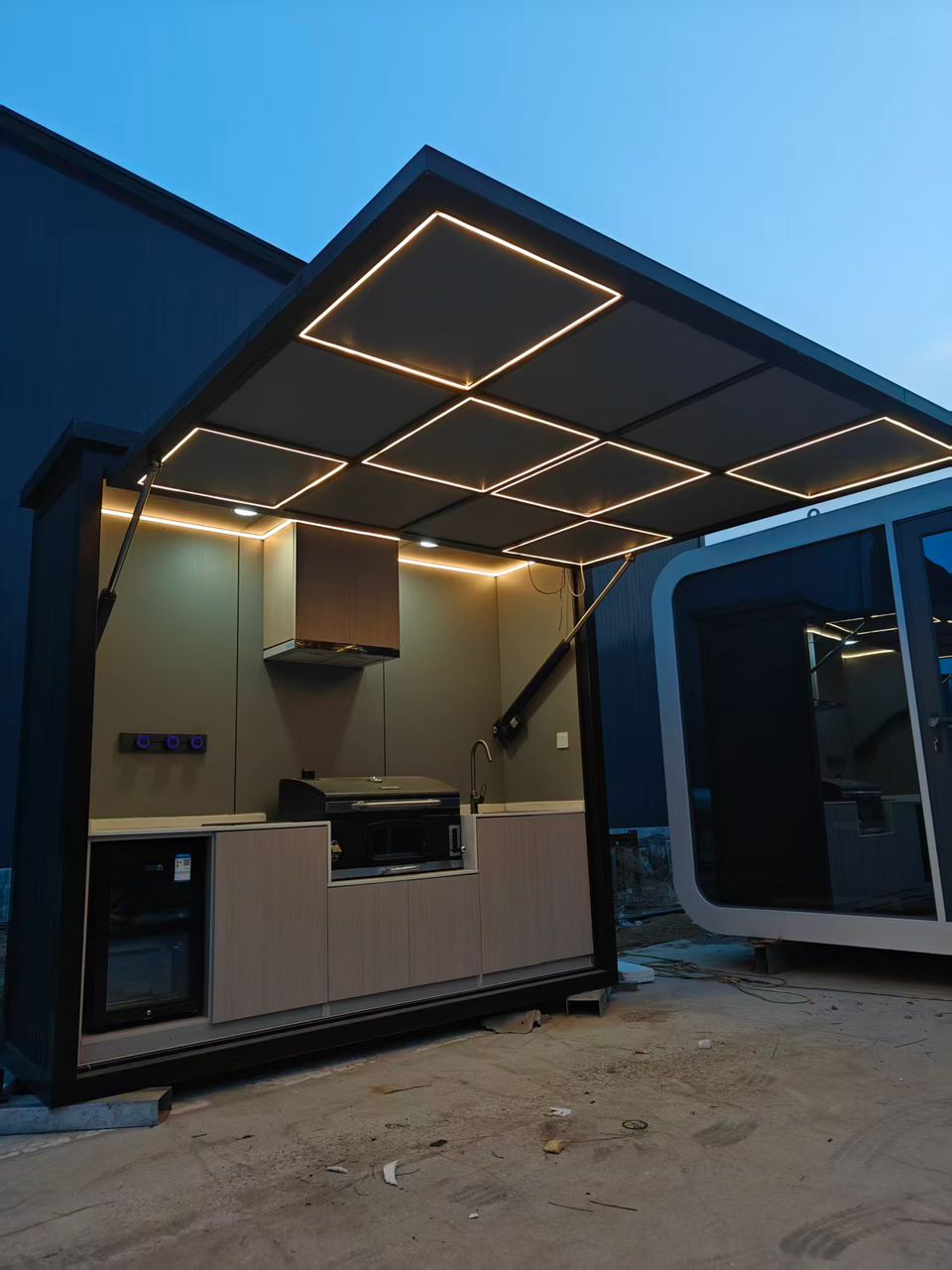 Modern outdoor kitchen with warm LED lighting and pizza oven